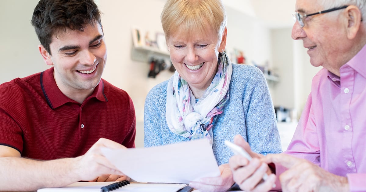 Young Man Helping Senior Couple With Financial Paperwork At Home